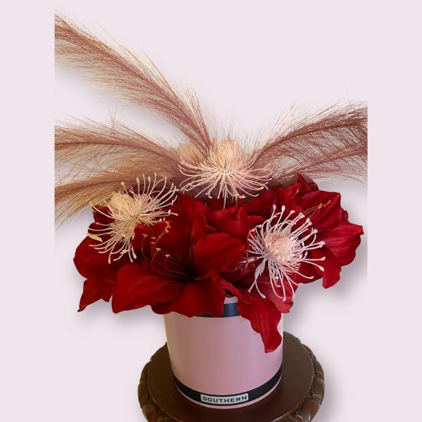 A flamboyant design with large dark red flowers, pink flowers for contrast and mauve feathery reeds in a purple vase