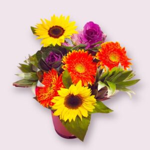 Bright yellow sunflowers amongst orange gerberas and purple cabbage flowers. Silver tree fern also featured.