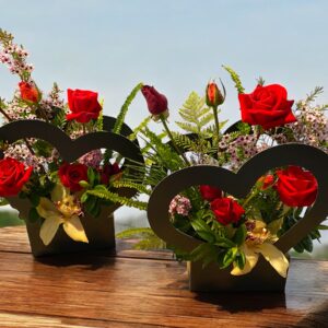 Two black cut out hearts with red roses, geraldton wax and green foilage extending out the hearts. A large orchid is centred in the middle of the two hearts