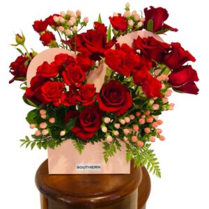 A large arrangement of red roses and pale pink berries encased in a heart shaped pale pink box