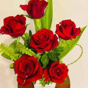 Red roses, curled fern and long green leaves within a white ceramic cube vase
