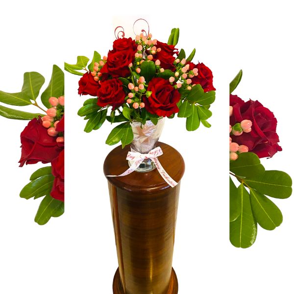 red rose and pale pink arrangement in glass vase on stand