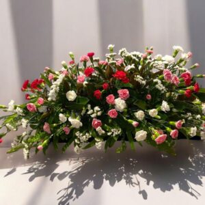 Simple yet stylish casket spray with light and dark pink carnations, with a mix of white flowers