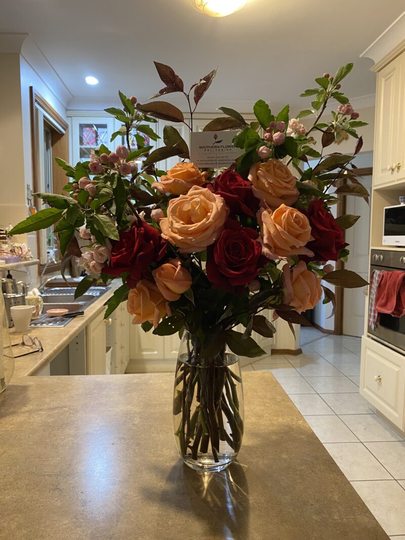 Tall arrangement of apricot and red roses with long green foilage