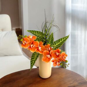 Bright orange orchids displayed on an angle with tropical leaves. An artificial arrangement.