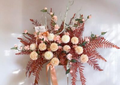 Tall artificial modern arrangement with rust foilage, apricot and white flowers, dash of pink blossom and a white branch sprig in a tall white vase